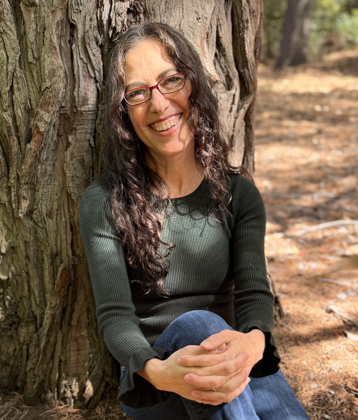 Asha Goldstein, LCSW, sitting against a tree trunk outdoors